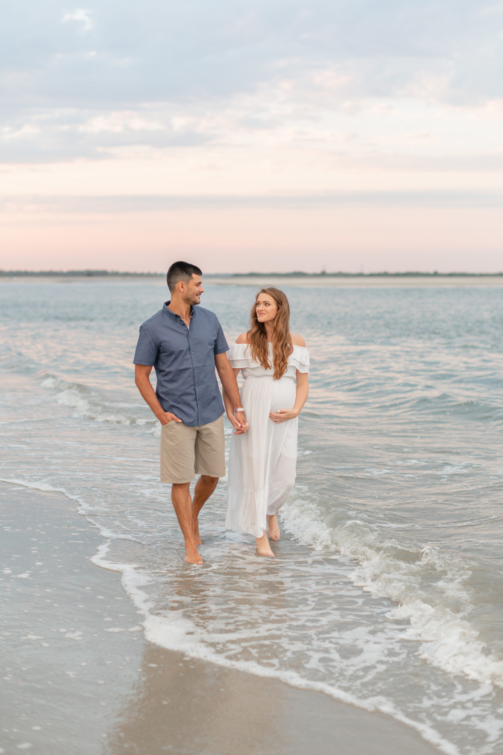 husband and wife walking on a Charleston beach at sunset celebrating their maternity session